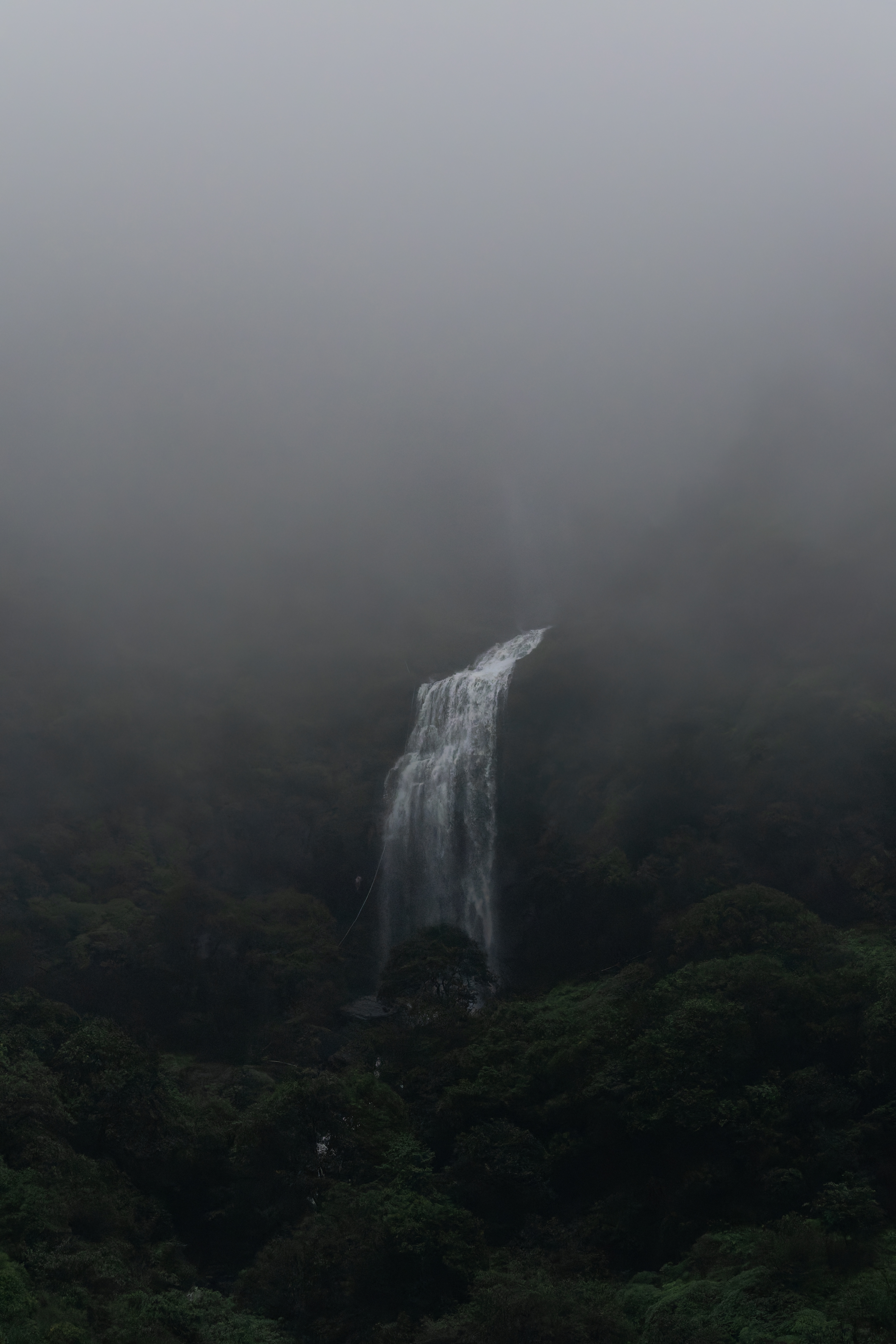 A seasonal waterfall near Mahabaleshwar shrouded in heavy mist and fog under dark, moody light