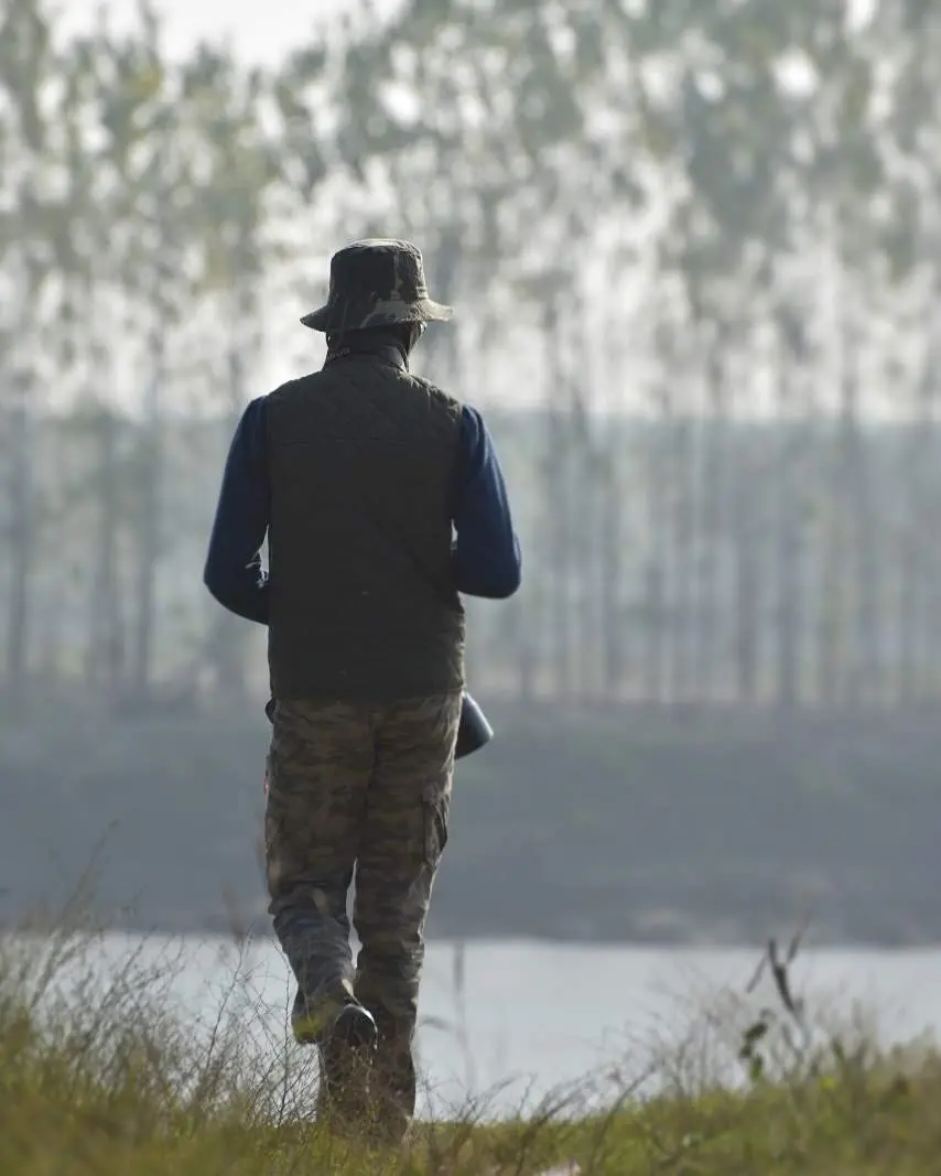 Arjun, turned away from the camera in a wildlife hat and holding a camera, birding on the Sutlej riverbed